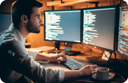 Focused young developer coding late in office writing script shown on computer monitors, serious handsome coder programmer hacker programming developing software applications working alone at night