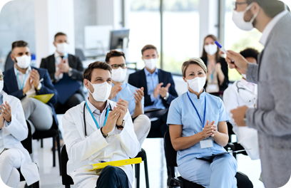 Large group of doctors and business people with protective face masks applauding while attending an educational event at conference hall. Focus is on male doctor.