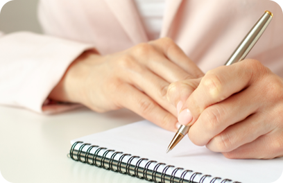 Closeup image of a woman writing down on a white blank notebook on wooden table. Pink background, selective focus. Business and education concept.