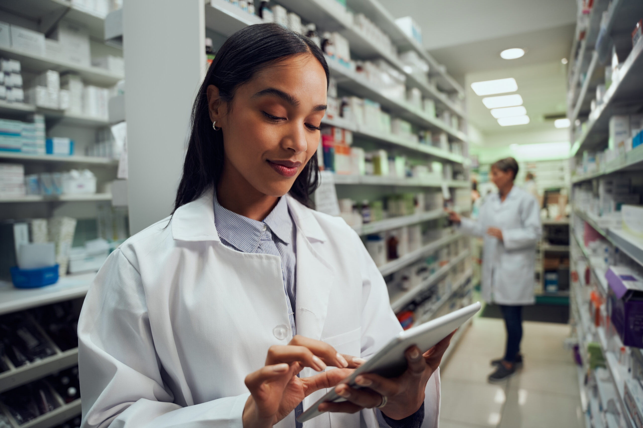 Smiling young female worker in pharmacy checking inventory using digital tablet