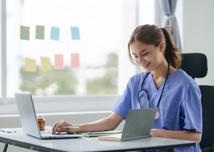 Attentive nurse in scrubs reviewing medical history or patient information on her laptop in office