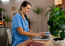 Female medical intern in blue medical scrubs e-learning on laptop at the ordination