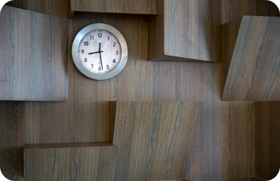 Clock over dark background with copy space. The extruded pieces of the wall may give the concept of time pressure. Modern office with wooden wall.