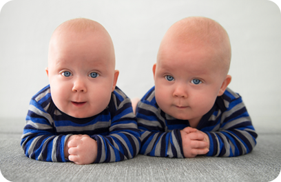 Identical twins lying down on grey mattress