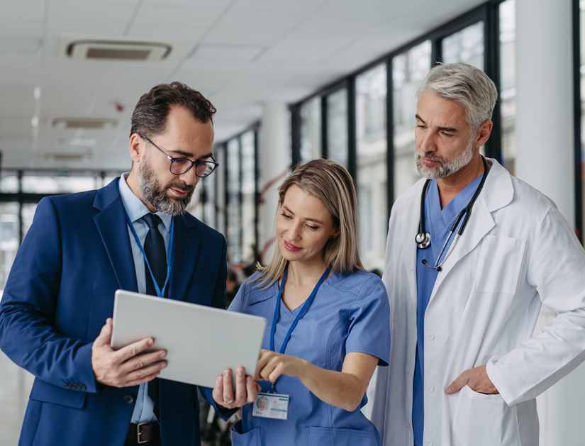 Pharmaceutical sales representative talking with doctors in medical building, presenting new product on tablet. Hospital director, manager in private medical clinic handshaking with doctors.