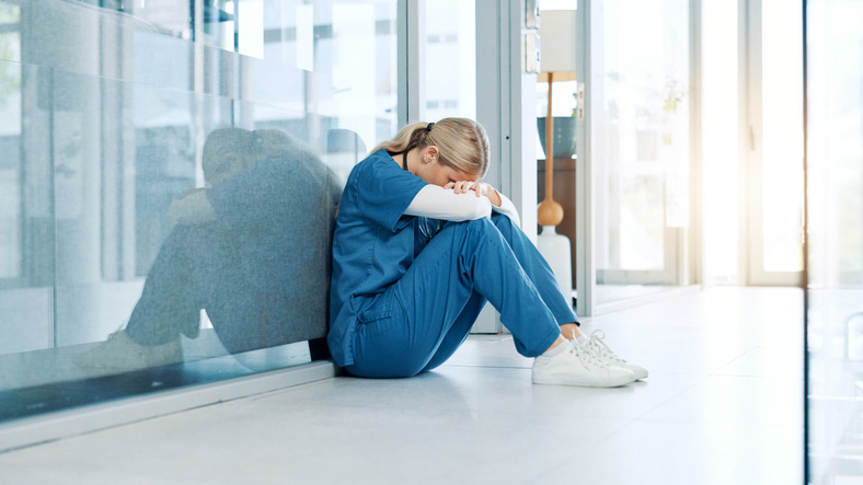 Healthcare, nurse and stress on floor in hospital hallway with bad news, treatment fail and regret.