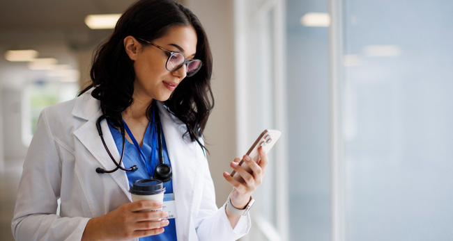 Smiling doctor with coffee cup and smartphone in modern hospital