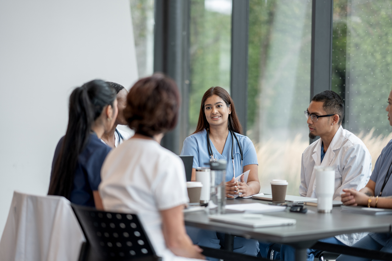 A diverse group of medical professionals gathers in a meeting room, engaging in a collaborative discussion about patient care strategies, fostering teamwork and ensuring quality healthcare in a bright and modern environment.